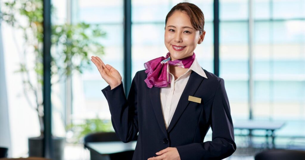 スーツを着た女性が右手を挙げつつご案内しますと表現している