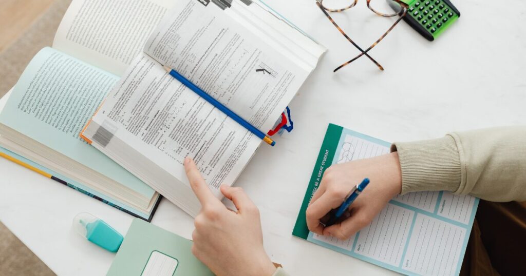 デスクで勉強している様子を上から映している。テキスト、ノート、テキストを指さす手